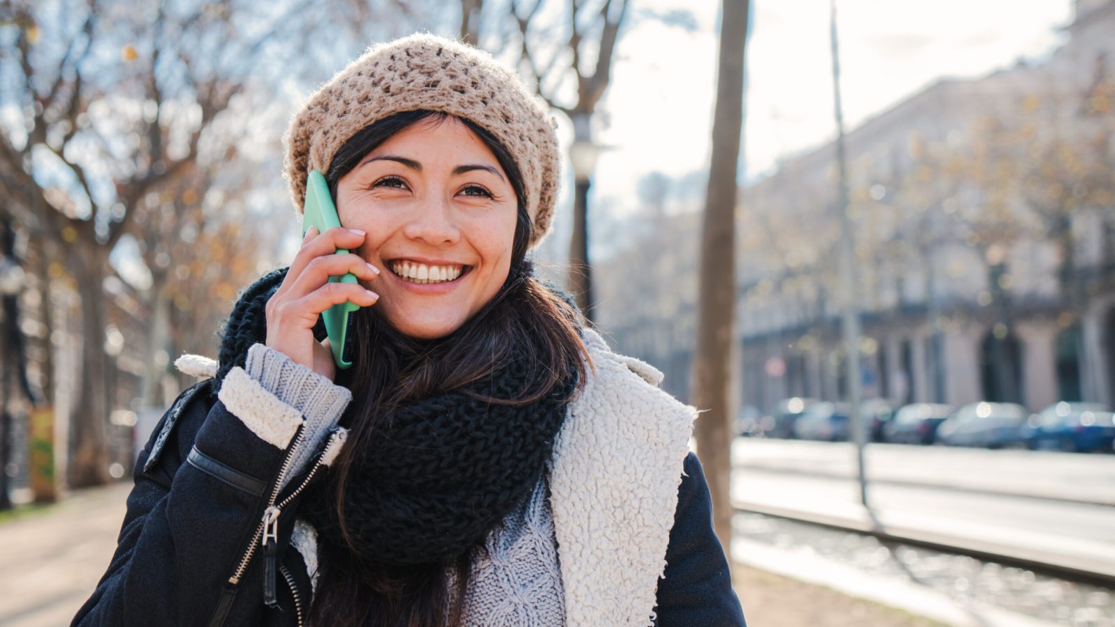 Young happy woman having a mobile phone call outdoors. One asian female smiling and talking by cellphone. Cheerful lady using a smartphone to have a conversation wearing hat and coat. communication. High quality photo